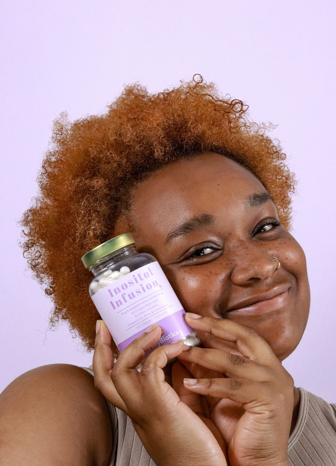 Red headed black woman, holding a bottle of inositol infusion plus. She is smiling. PCOS