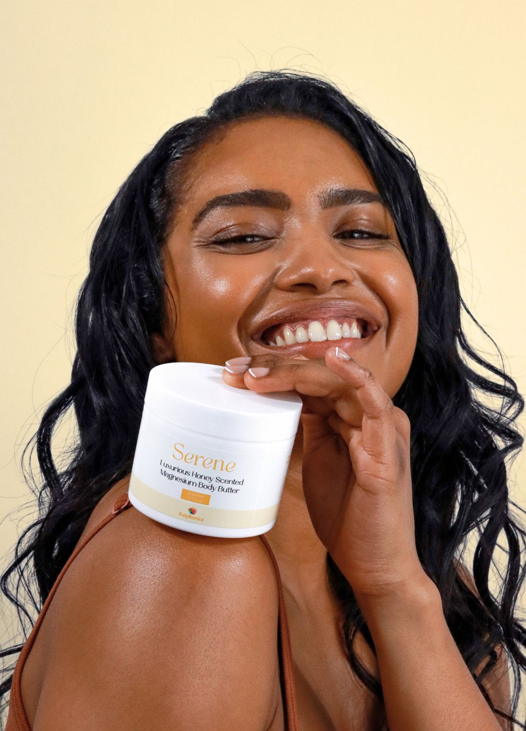 Asian lady with deep skin tone holding serene magnesium body butter from polybiotics with a pale yellow background